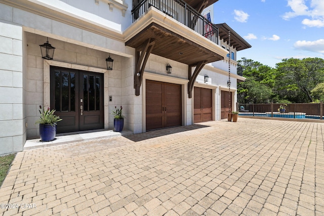 entrance to property with a balcony, a fenced in pool, french doors, and a garage