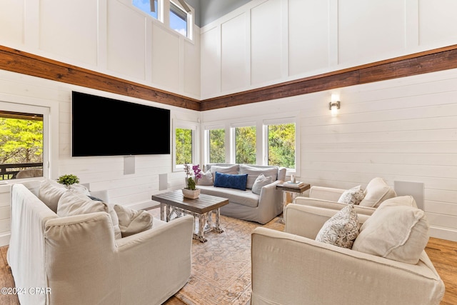 living room with a high ceiling, wood walls, light hardwood / wood-style floors, and a healthy amount of sunlight