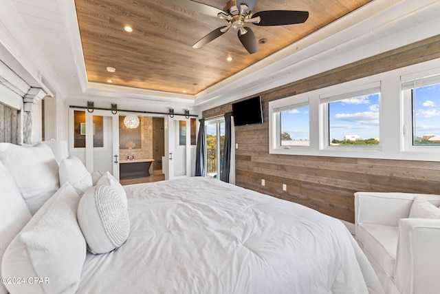 bedroom with wooden walls, a raised ceiling, a barn door, and multiple windows