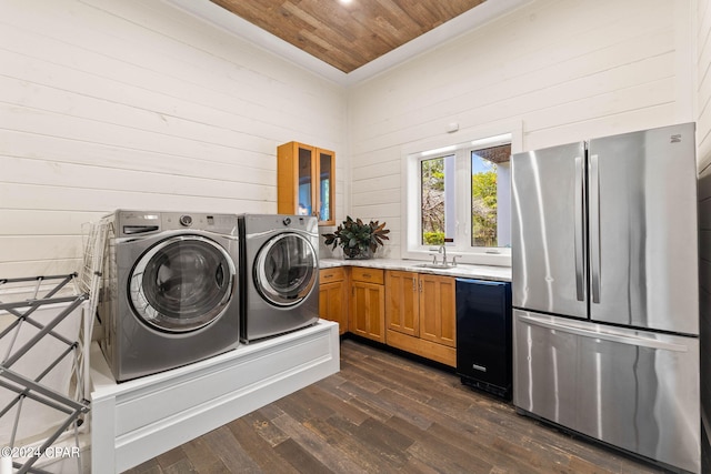 laundry room with wood ceiling, dark hardwood / wood-style floors, sink, wood walls, and washer and clothes dryer