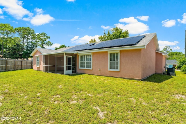 rear view of house featuring a sunroom, solar panels, and a lawn