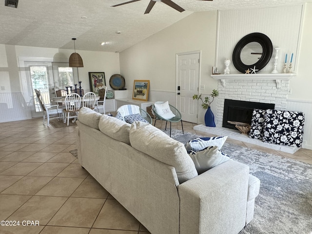 living room with vaulted ceiling, a textured ceiling, light tile patterned floors, ceiling fan, and a fireplace