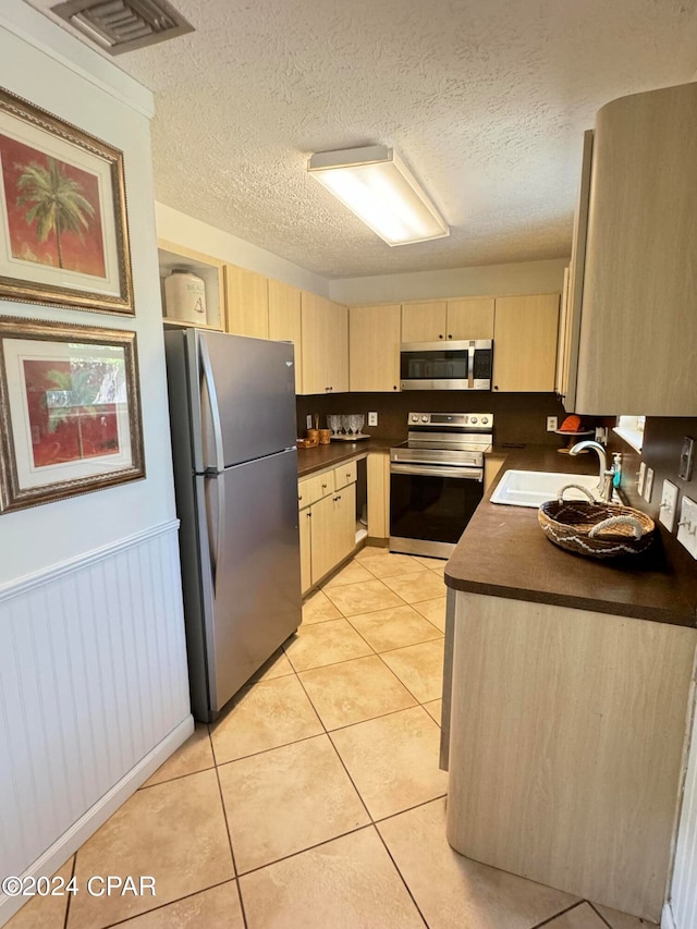 kitchen featuring sink, appliances with stainless steel finishes, a textured ceiling, and light tile patterned floors