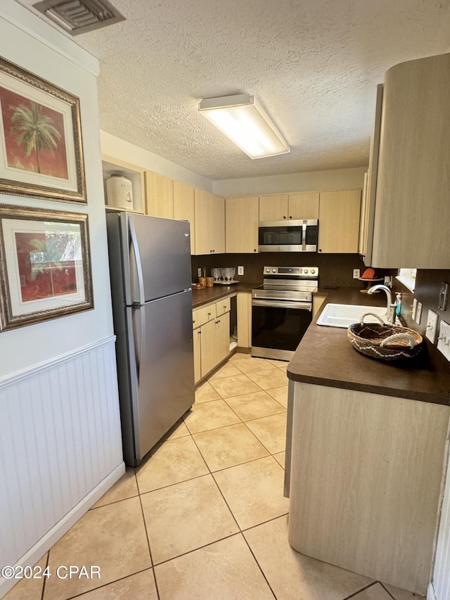 kitchen with sink, light tile patterned floors, stainless steel appliances, a textured ceiling, and light brown cabinetry