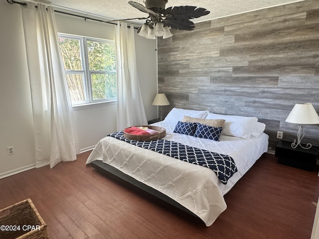 bedroom featuring ceiling fan, dark wood-type flooring, wooden walls, and a textured ceiling