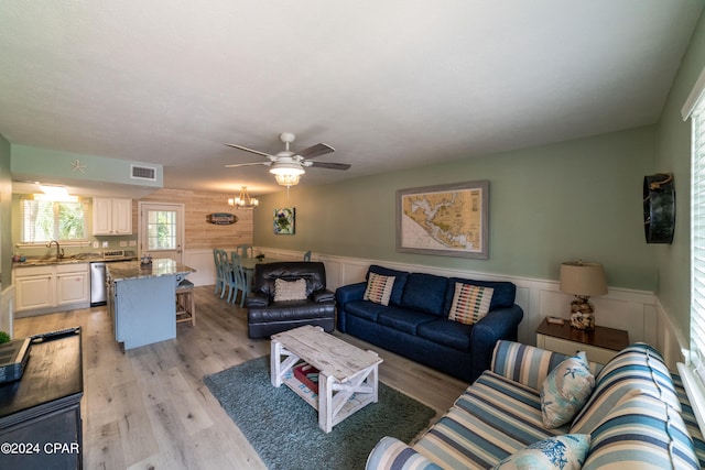 living room featuring light hardwood / wood-style floors, wooden walls, sink, and ceiling fan