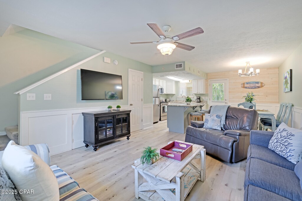135 Robin Ln, Panama City Beach, FL 32407 - living area featuring a chandelier, light wood finished floors, ceiling fan, wainscoting, and a decorative wall