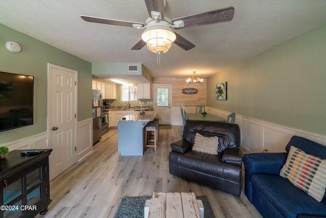 living room with ceiling fan with notable chandelier, light hardwood / wood-style floors, and sink