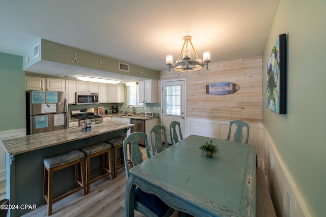 dining space featuring light hardwood / wood-style flooring, sink, a textured ceiling, a chandelier, and wood walls