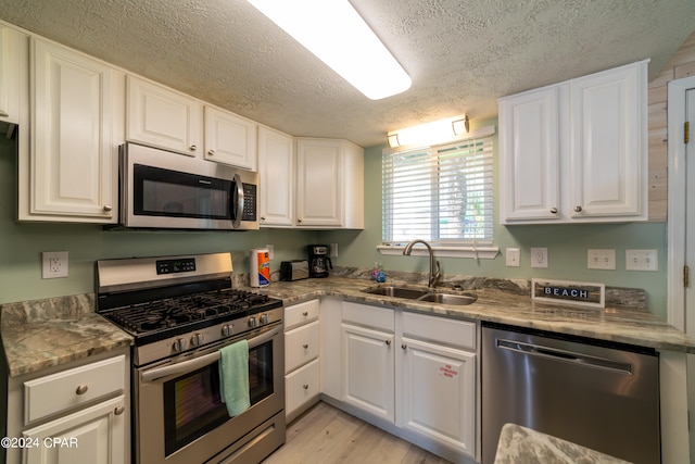 kitchen with stainless steel appliances, white cabinets, sink, light hardwood / wood-style floors, and a textured ceiling