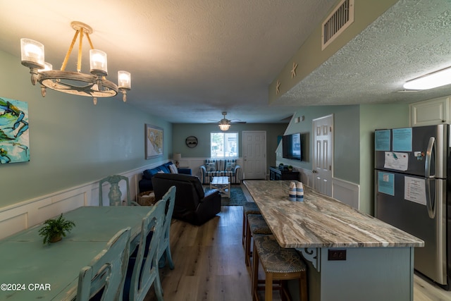 kitchen featuring stainless steel fridge, pendant lighting, light wood-type flooring, ceiling fan with notable chandelier, and a textured ceiling