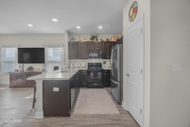 kitchen with sink, light hardwood / wood-style flooring, a kitchen breakfast bar, and black appliances