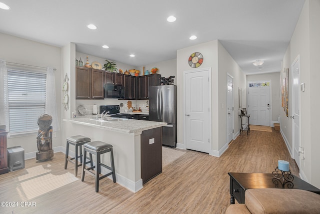 kitchen featuring dark brown cabinets, black appliances, light hardwood / wood-style floors, kitchen peninsula, and a kitchen breakfast bar