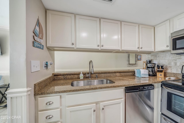 kitchen featuring backsplash, dark stone counters, sink, appliances with stainless steel finishes, and white cabinetry