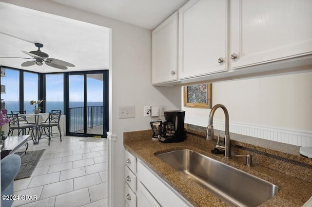 kitchen featuring a water view, white cabinetry, dark stone counters, and sink