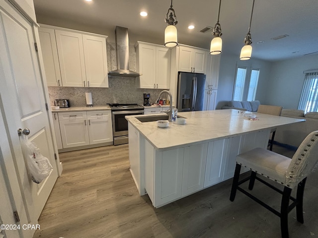 kitchen with light hardwood / wood-style flooring, white cabinets, appliances with stainless steel finishes, wall chimney exhaust hood, and sink