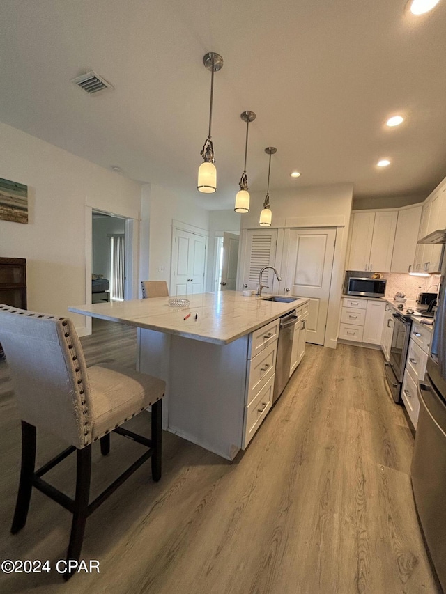 kitchen featuring light hardwood / wood-style flooring, stainless steel appliances, a center island with sink, decorative light fixtures, and a kitchen breakfast bar