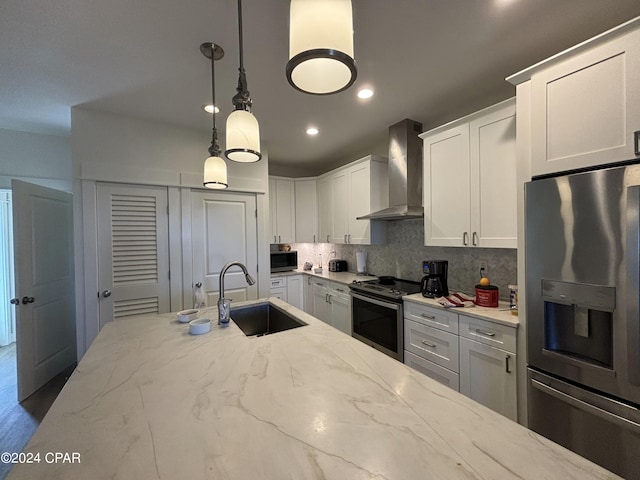 kitchen featuring tasteful backsplash, wall chimney range hood, stainless steel appliances, pendant lighting, and sink