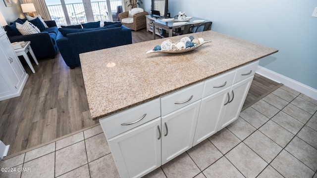 kitchen featuring white cabinetry, light hardwood / wood-style flooring, a kitchen island, and light stone counters