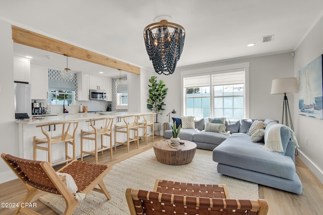 living room with sink, a notable chandelier, light hardwood / wood-style floors, and ornamental molding