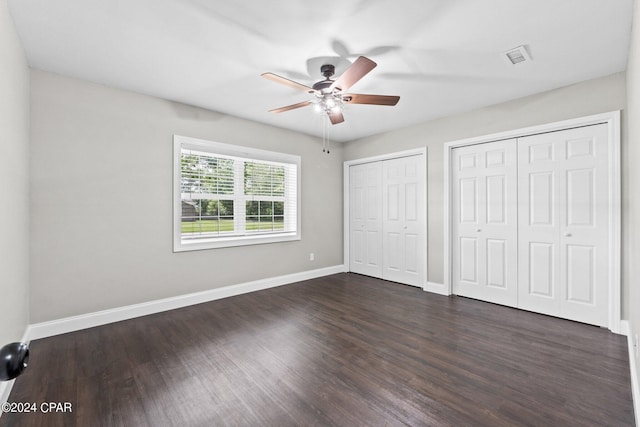 unfurnished bedroom with ceiling fan, dark wood-type flooring, and multiple closets