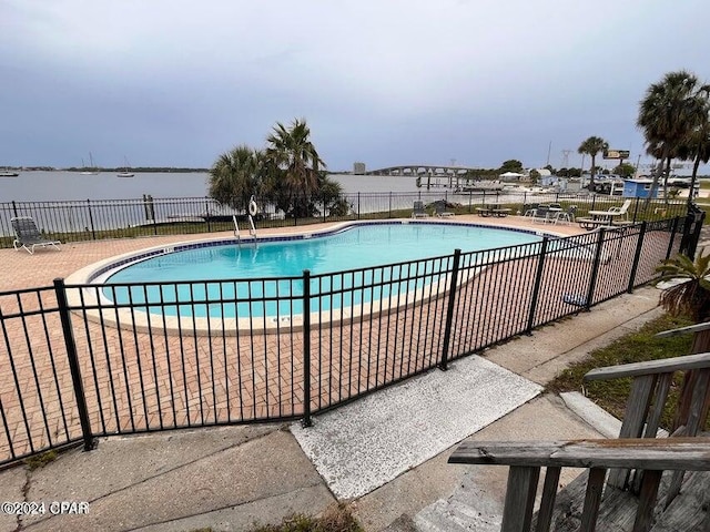 pool featuring a water view, fence, and a patio