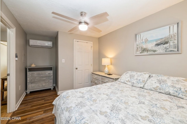 bedroom featuring a wall unit AC, dark wood finished floors, a ceiling fan, and baseboards