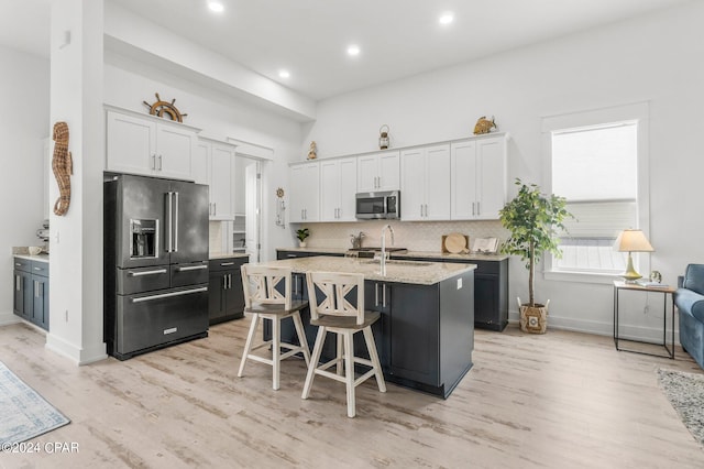 kitchen with a breakfast bar area, stainless steel appliances, decorative backsplash, light wood-type flooring, and an island with sink