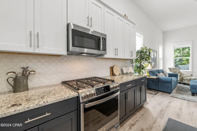 kitchen with white cabinetry, tasteful backsplash, light stone counters, light hardwood / wood-style floors, and appliances with stainless steel finishes