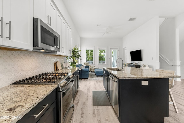 kitchen featuring white cabinets, light wood-type flooring, a center island with sink, appliances with stainless steel finishes, and backsplash