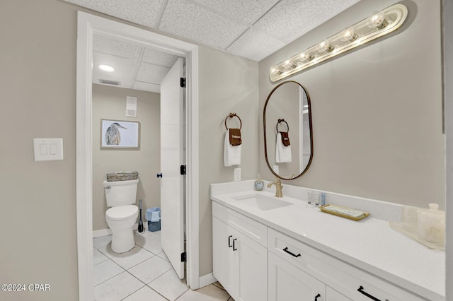 bathroom with tile patterned flooring, vanity, a drop ceiling, and toilet