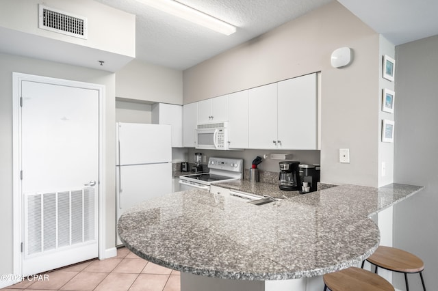 kitchen featuring white appliances, white cabinets, kitchen peninsula, a kitchen breakfast bar, and light tile patterned flooring