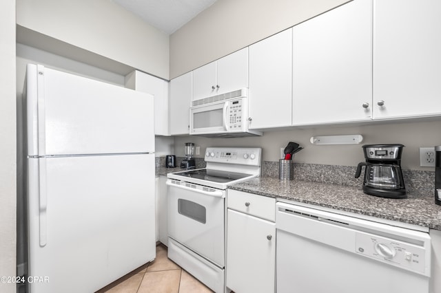 kitchen featuring dark stone counters, white appliances, light tile patterned floors, and white cabinets