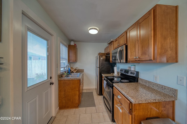 kitchen featuring baseboards, brown cabinets, stainless steel appliances, a sink, and light tile patterned flooring