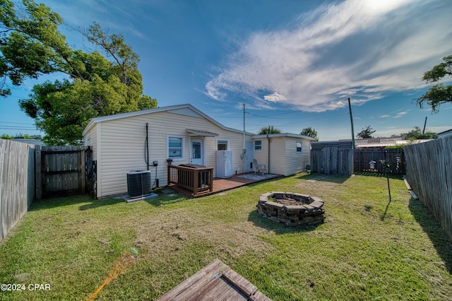 back of house featuring a deck, an outdoor fire pit, a fenced backyard, cooling unit, and a lawn