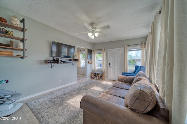 living room with light tile patterned floors, ceiling fan, baseboards, and a textured ceiling