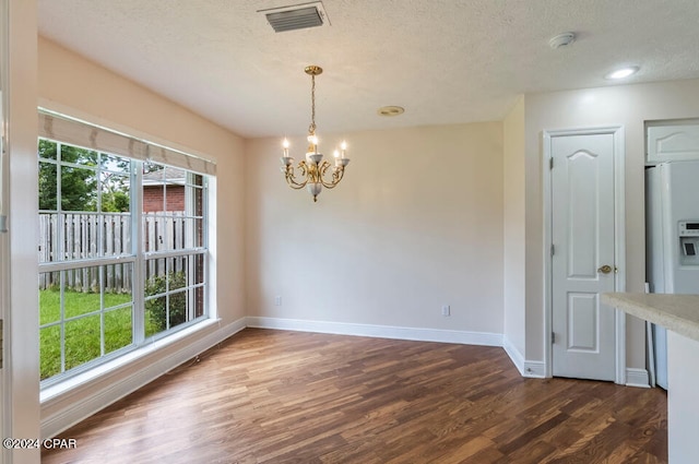 unfurnished dining area with a textured ceiling, a notable chandelier, and dark hardwood / wood-style flooring