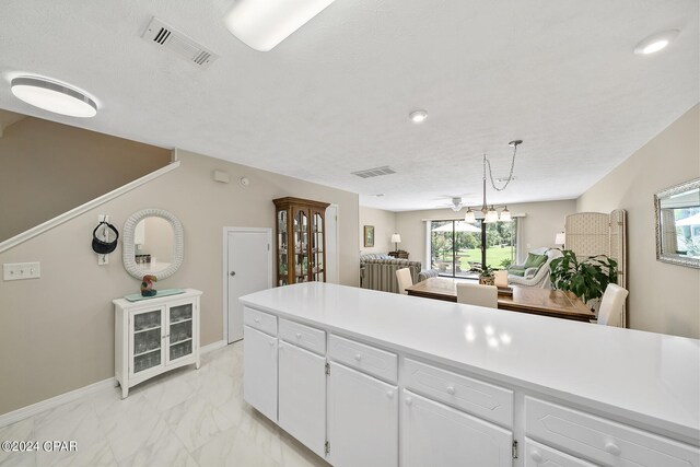 kitchen featuring pendant lighting, white cabinetry, a textured ceiling, and a notable chandelier