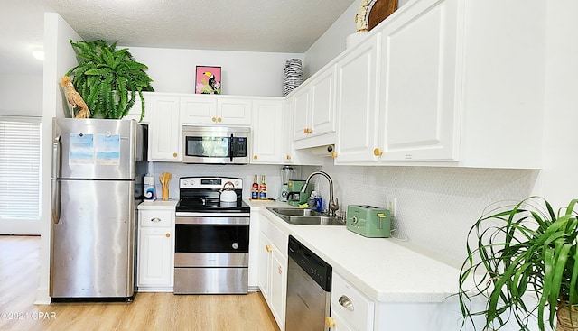 kitchen featuring light wood-type flooring, sink, white cabinets, stainless steel appliances, and backsplash