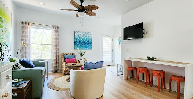 living room featuring light hardwood / wood-style flooring, ceiling fan, and a textured ceiling