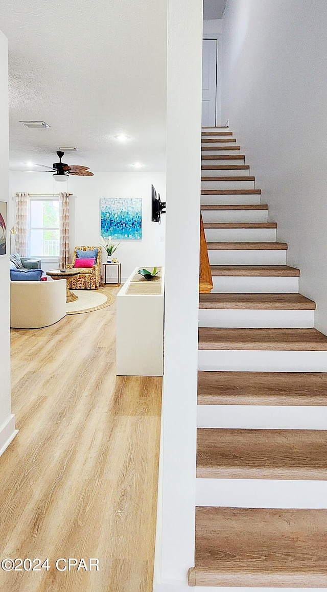 stairs with ceiling fan, a textured ceiling, and hardwood / wood-style floors