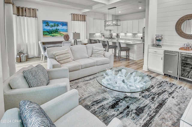 living area featuring recessed lighting, beverage cooler, light wood-type flooring, beam ceiling, and an inviting chandelier