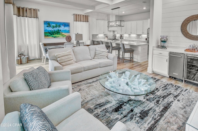 living room featuring beam ceiling, a notable chandelier, light wood-type flooring, and beverage cooler