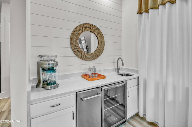 bar with wine cooler, wooden walls, white cabinetry, light hardwood / wood-style flooring, and sink