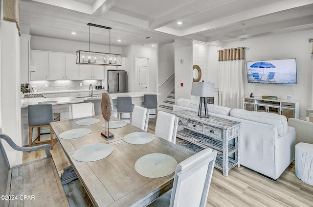 dining space with beam ceiling, light wood-type flooring, sink, and a chandelier