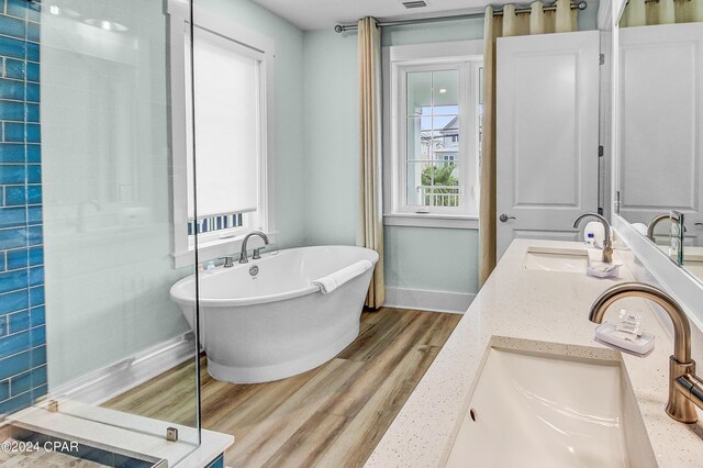 bathroom with dual vanity, wood-type flooring, and a tub to relax in