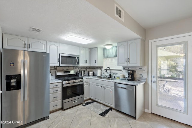 kitchen with appliances with stainless steel finishes, tasteful backsplash, a textured ceiling, sink, and white cabinetry