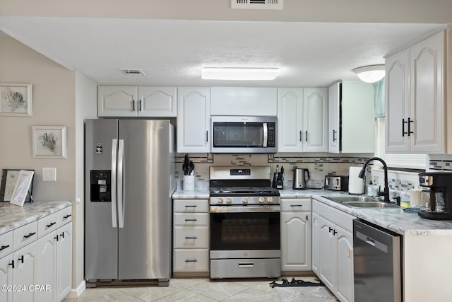 kitchen with sink, decorative backsplash, appliances with stainless steel finishes, light tile patterned flooring, and white cabinetry