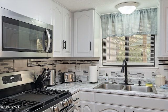 kitchen featuring sink, tasteful backsplash, a textured ceiling, white cabinets, and appliances with stainless steel finishes