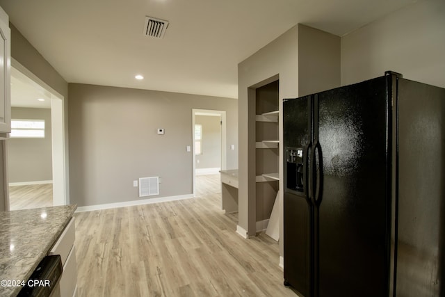 kitchen featuring white cabinetry, black fridge with ice dispenser, light stone countertops, and light wood-type flooring